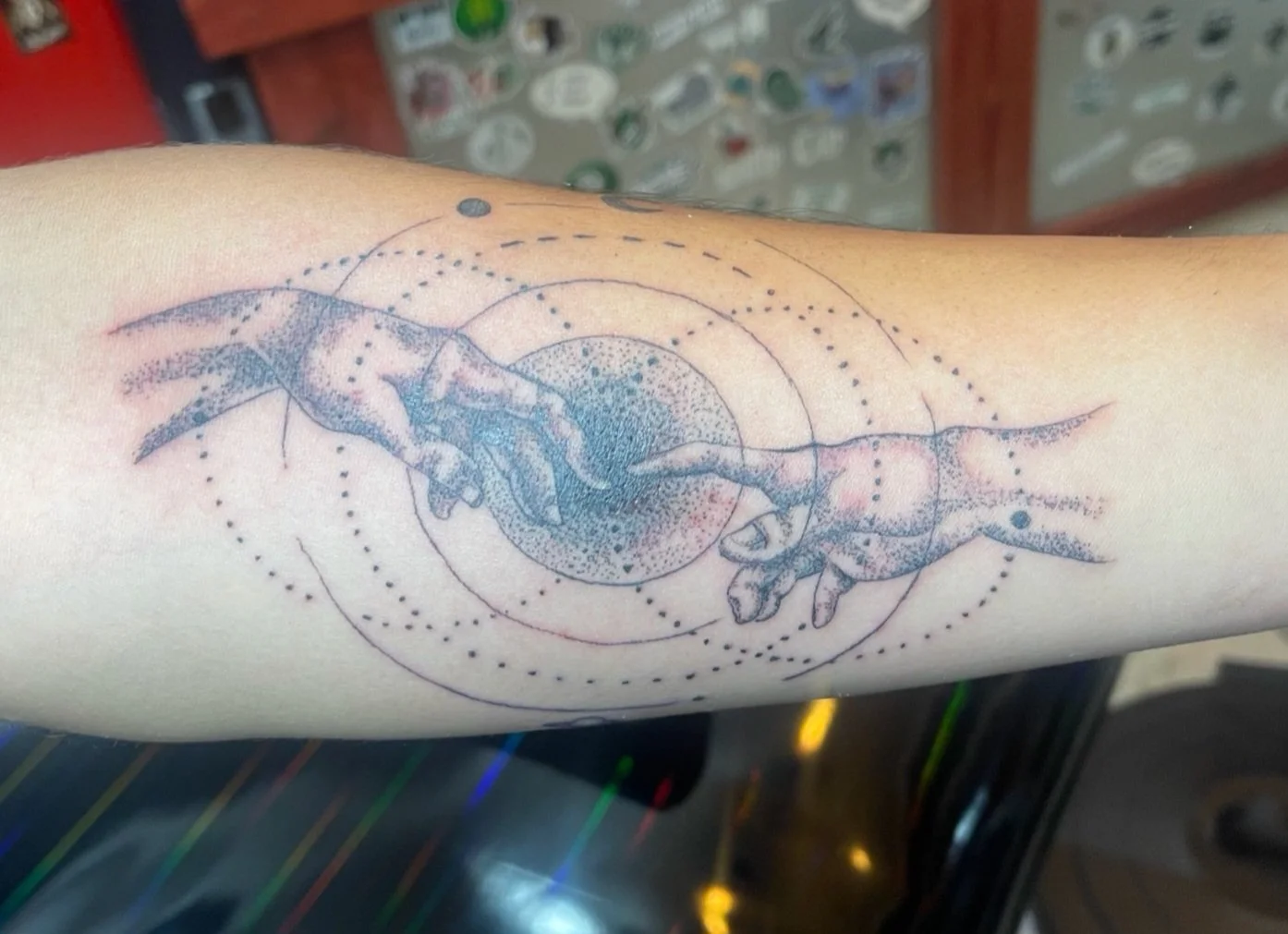 Tattoo of two hands reaching towards each other, inspired by Michelangelo's Creation of Adam, with dotted and circular design elements surrounding the hands.