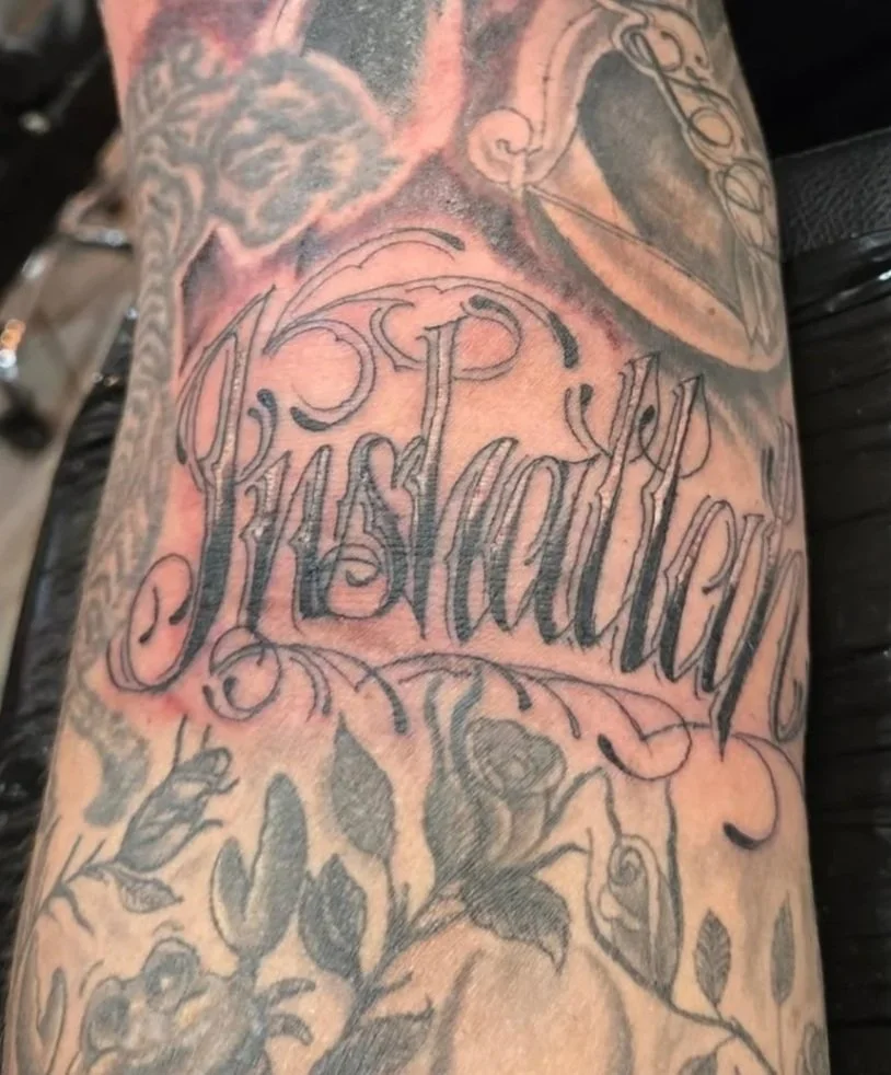 Tattoo of the word 'Traditional' in elaborate script surrounded by floral designs on a person's arm.