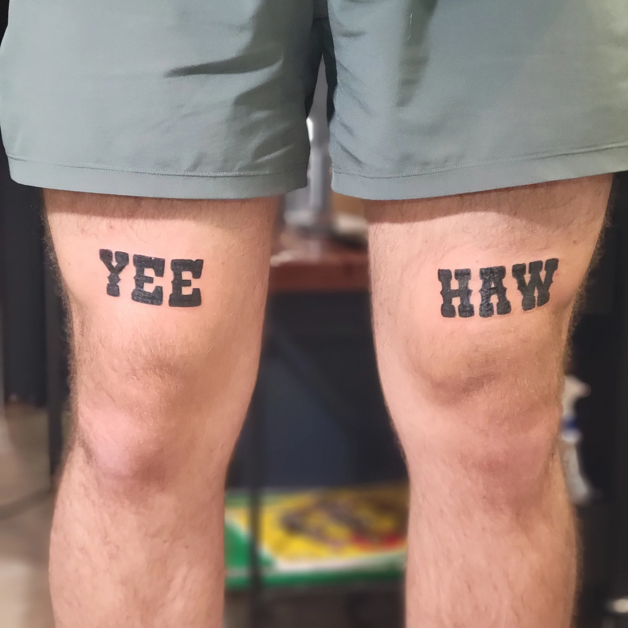 Tattooed words on a person's thighs that read 'YEE' on the left and 'HAW' on the right.