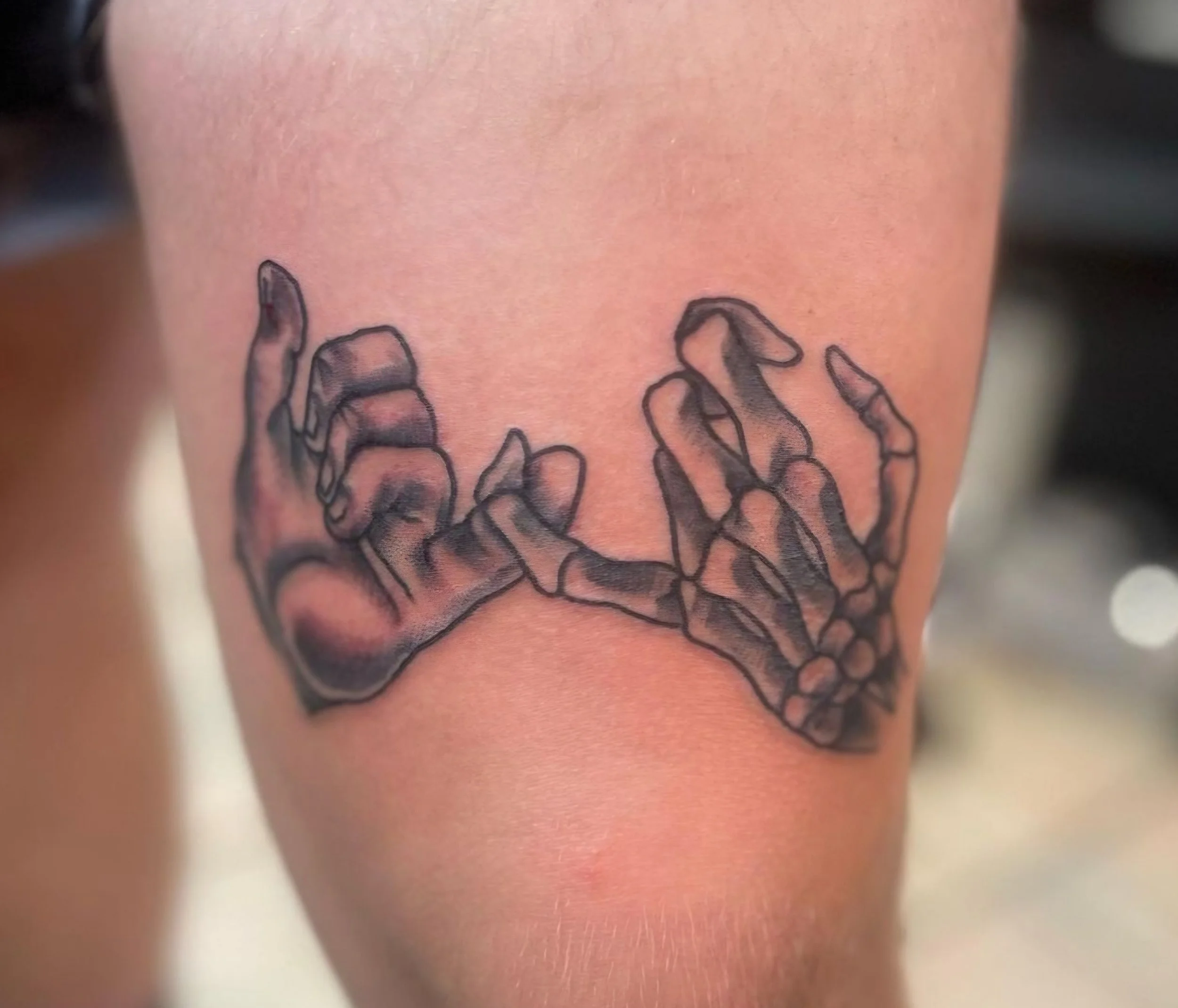 Tattoo of two skeletal hands making a pinky promise on person's thigh.