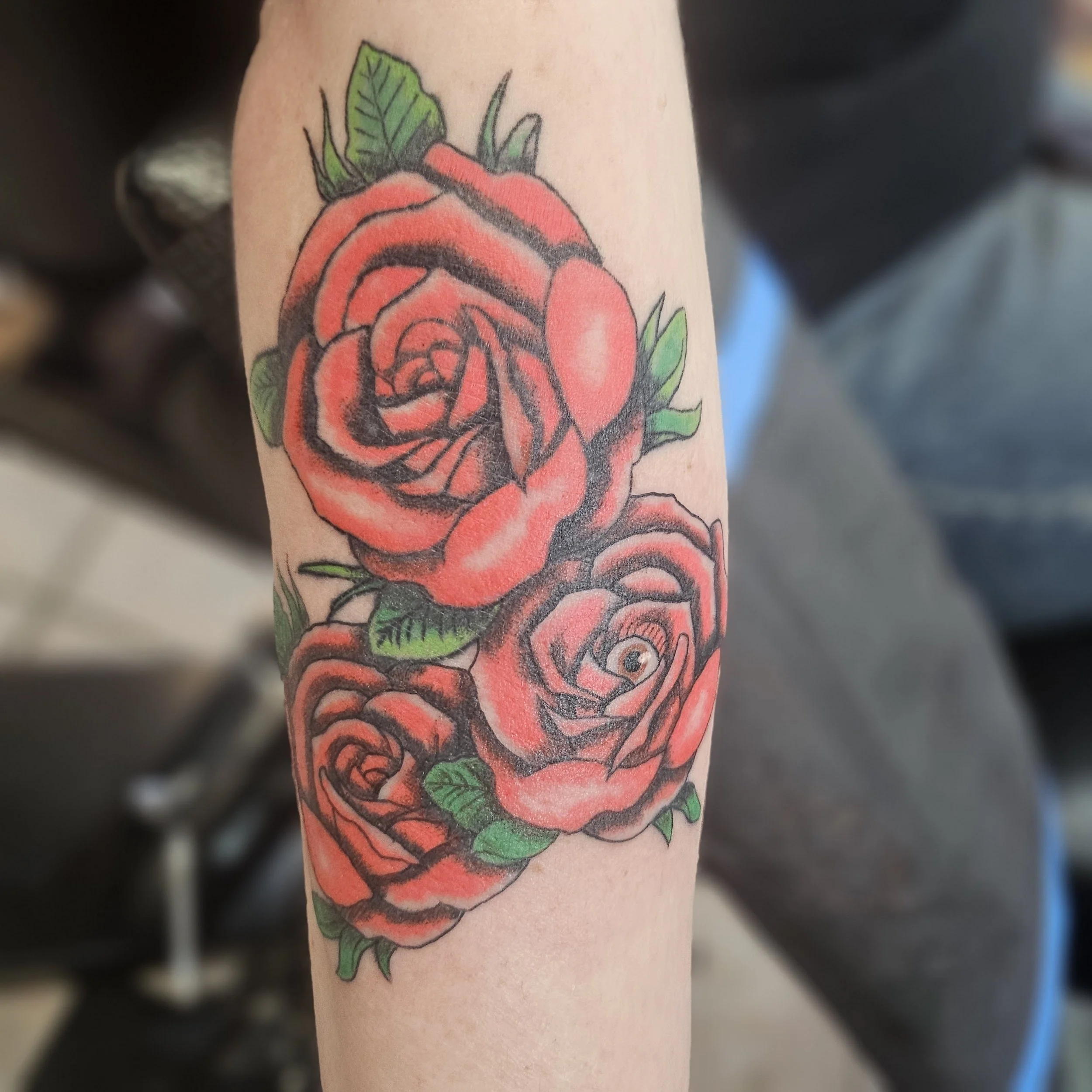 Tattoo of three red roses with green leaves on a person's forearm.