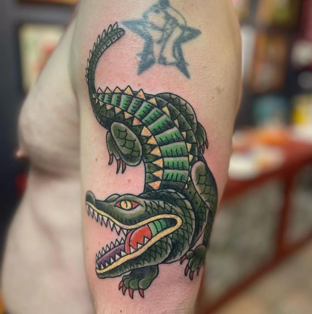 A tattoo of a green and black alligator with sharp teeth on a person's upper arm.