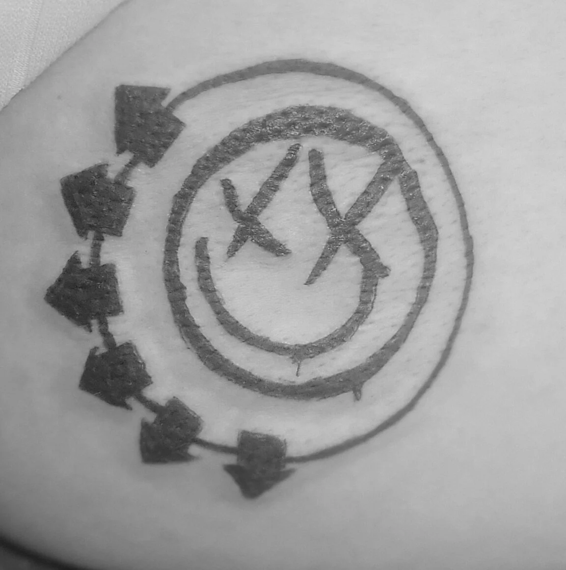A tattoo of a clock with Roman numerals, surrounded by arrows pointing clockwise, and additional decorative elements.