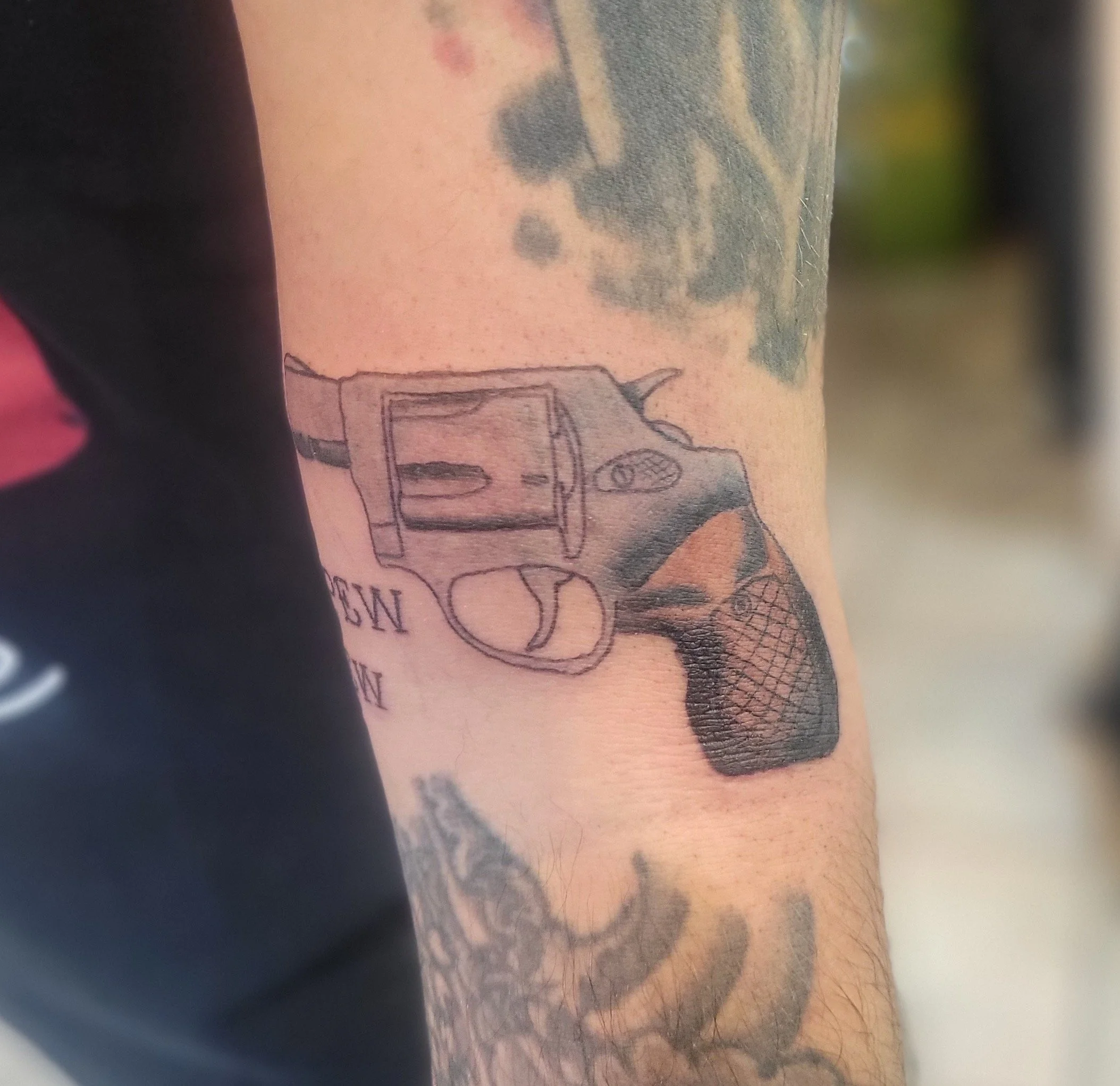 Tattoo of a semi-automatic handgun on a person's forearm, with some text below it.