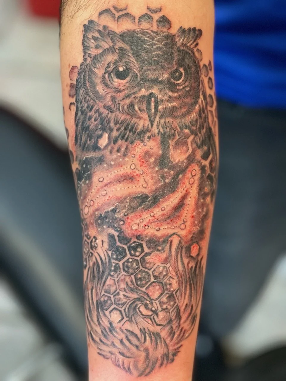Tattoo of an owl with detailed feathers, surrounded by hexagonal honeycomb patterns, with glowing effects and cosmic elements.