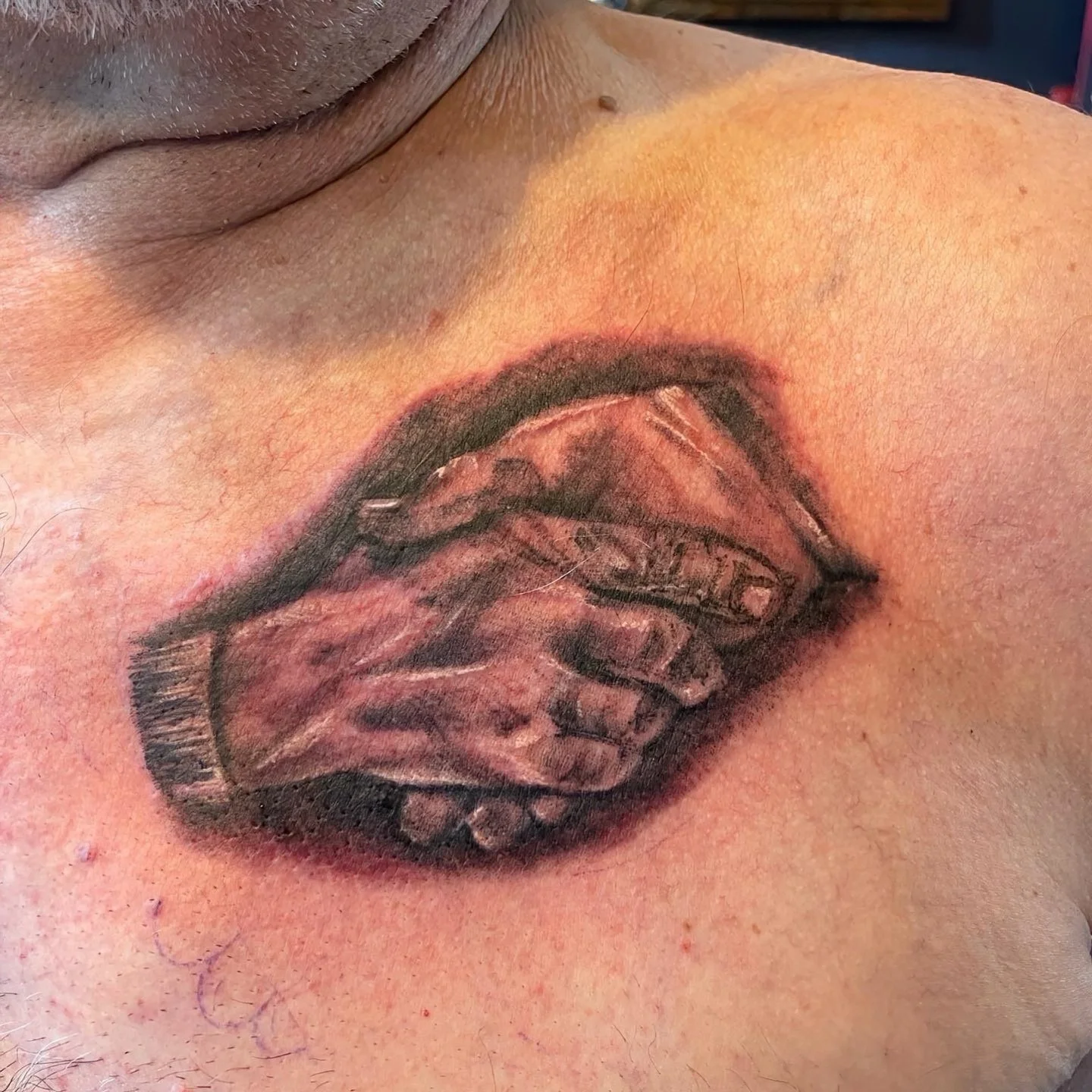 Tattoo of lips on a person's shoulder with smoke coming out of the mouth, in black and gray ink.