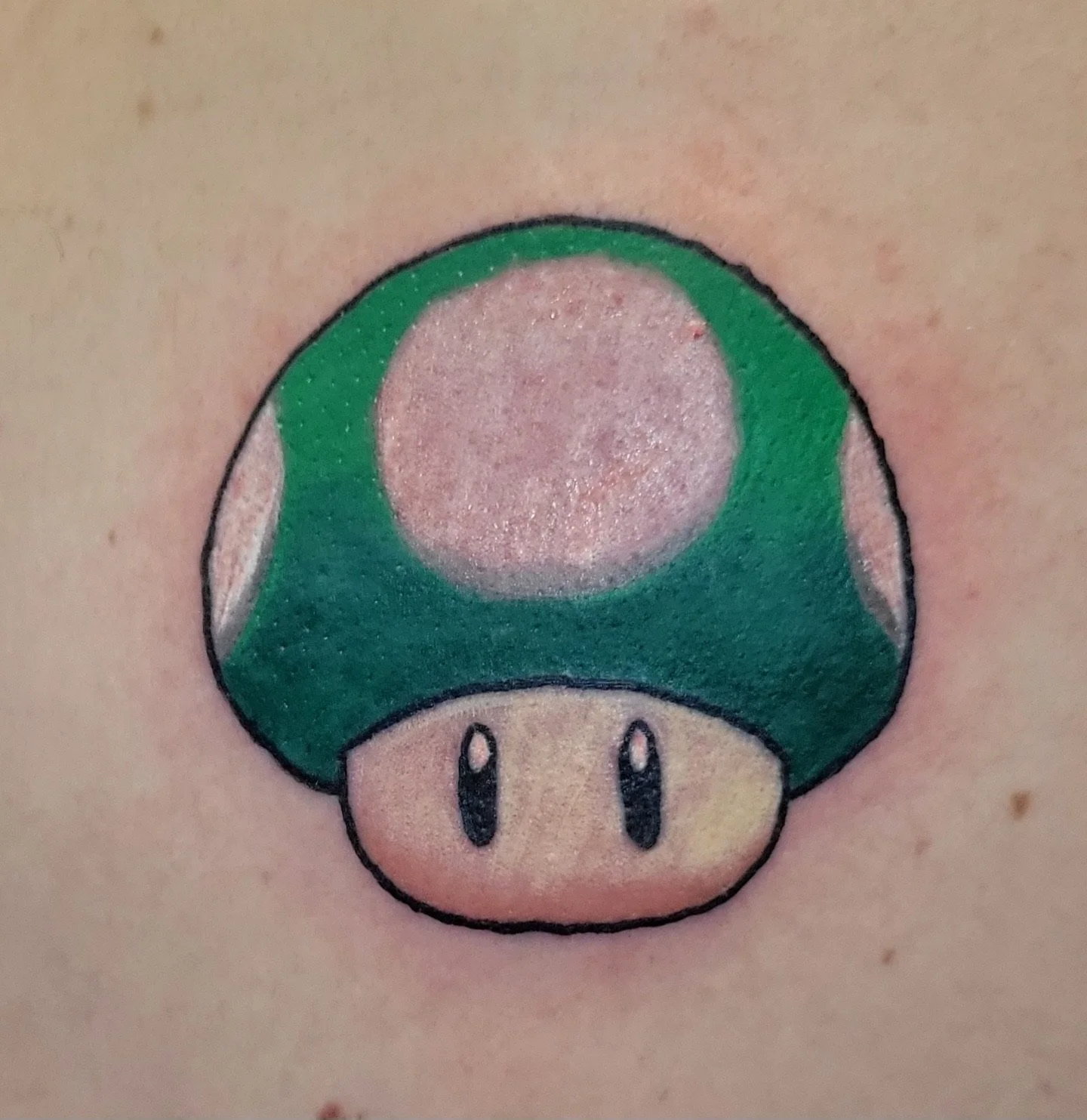 Tattoo of a green Super Mushroom from Mario on skin.