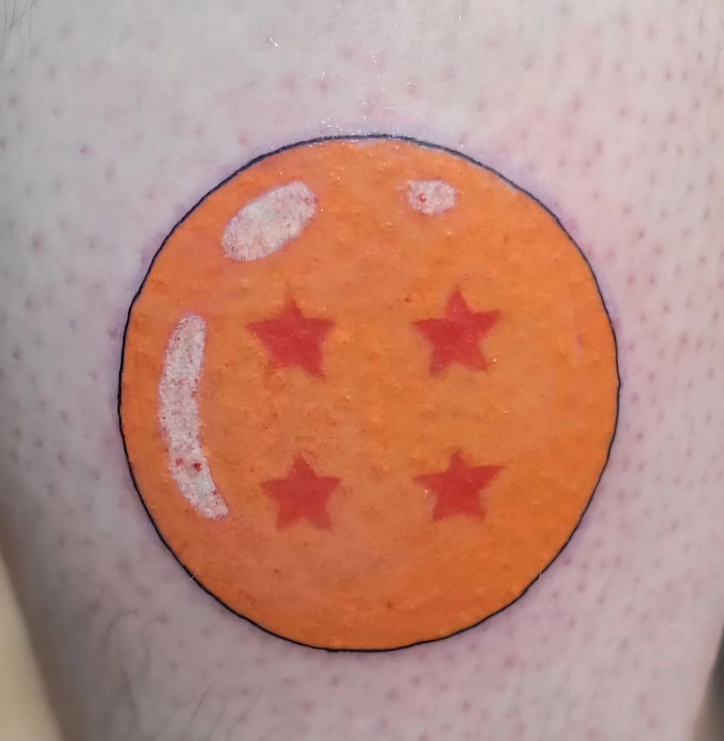 Tattoo of an orange circle with a smiley face, star eyes, and star-shaped mouth, outlined in black, on skin.