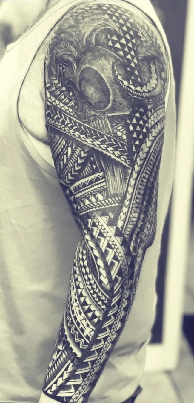 Black and gray tattoo sleeve featuring geometric patterns, tribal designs, and a portrait of a person's face.