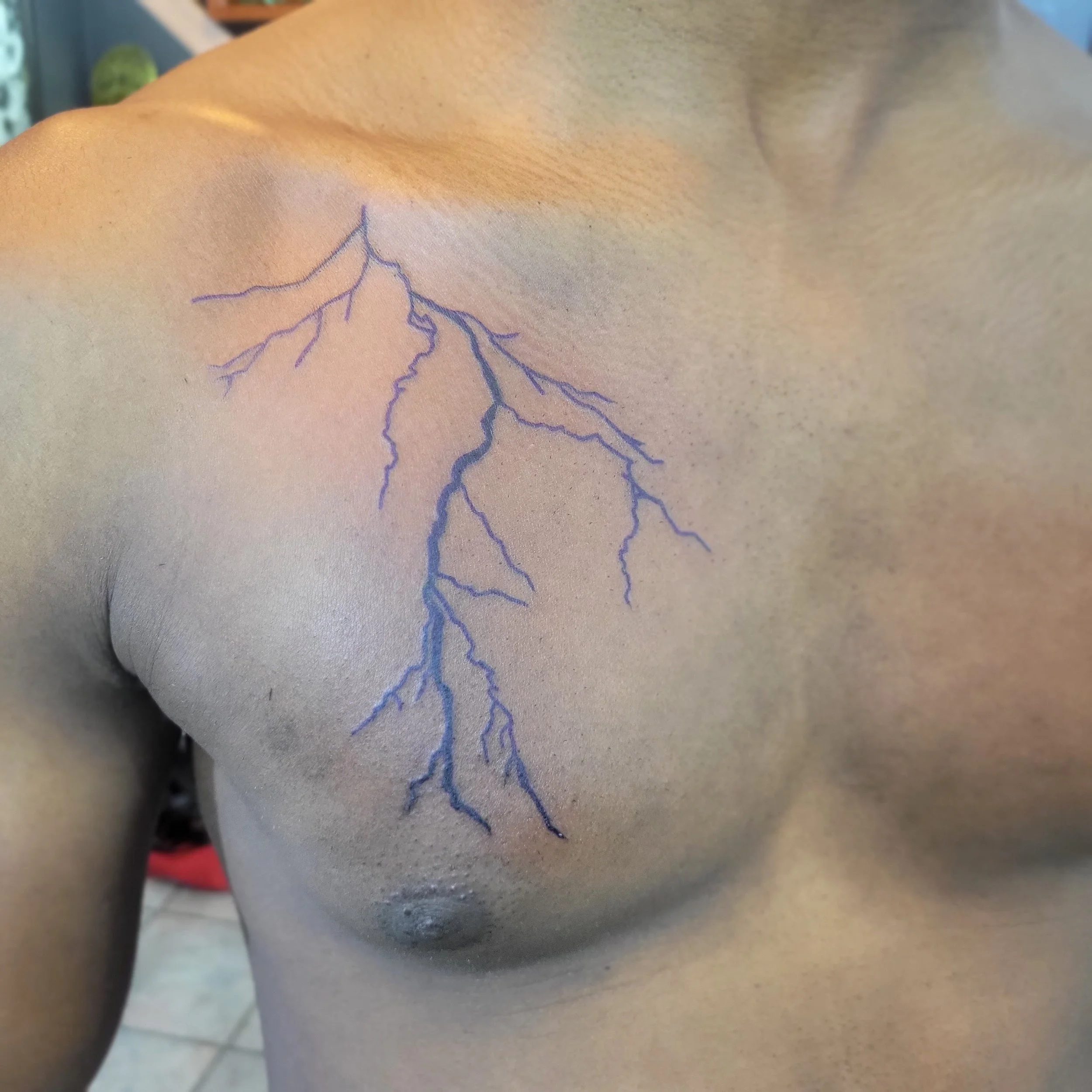 A tattoo of a blue lightning bolt on a person's chest, extending from the shoulder to the middle of the chest.