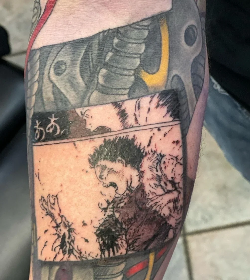 Black and white tattoo on a person's arm featuring a manga or comic style scene of a shouting man with spiky hair, with Japanese characters above.