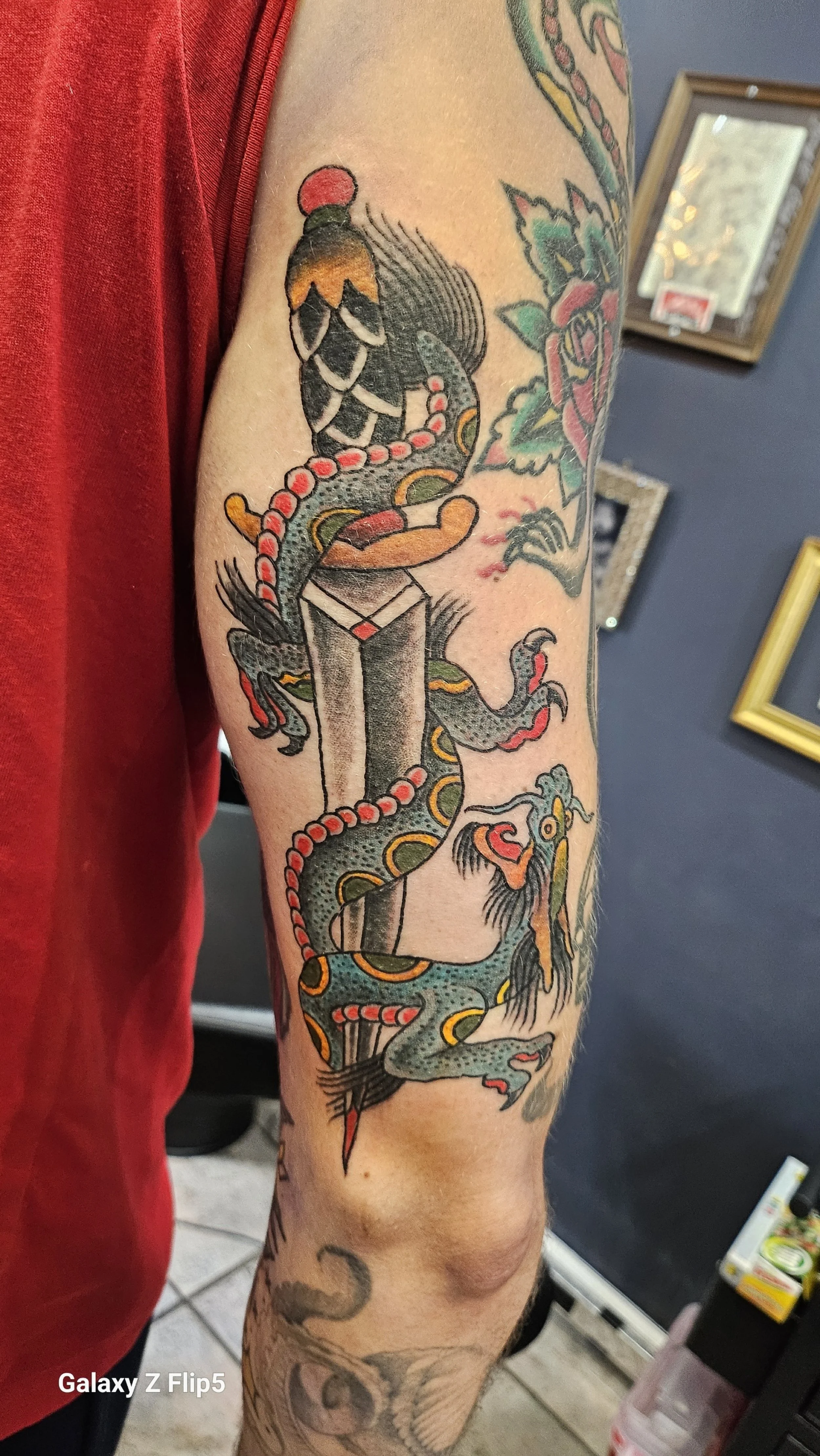 Tattoo of a koi fish and a dragon coiled around a traditional Japanese temple on a person's upper arm.