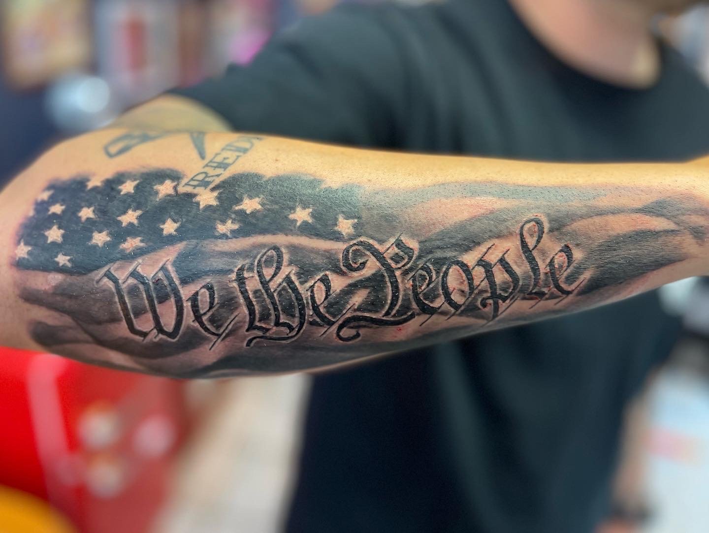 American pride forearm tattoo in black and grey with lettering.