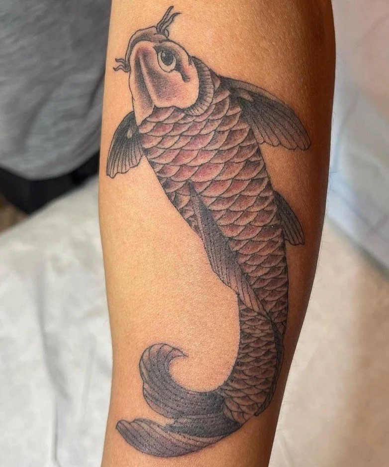 Tattoo of a fish with a human-like face on a person's arm.