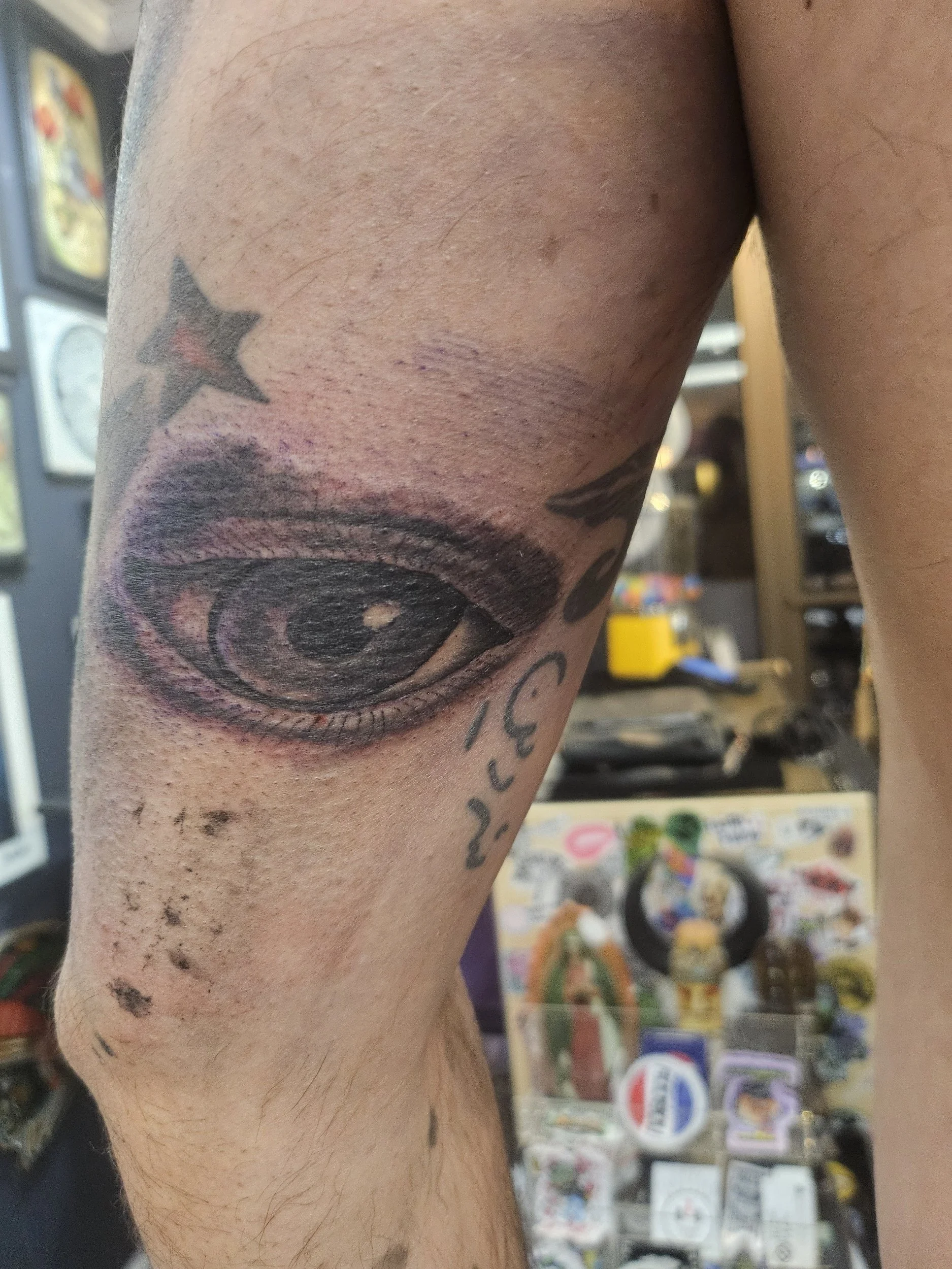 Tattoo of a realistic eye on a person's upper leg, with additional tattoos of a star and some text nearby.
