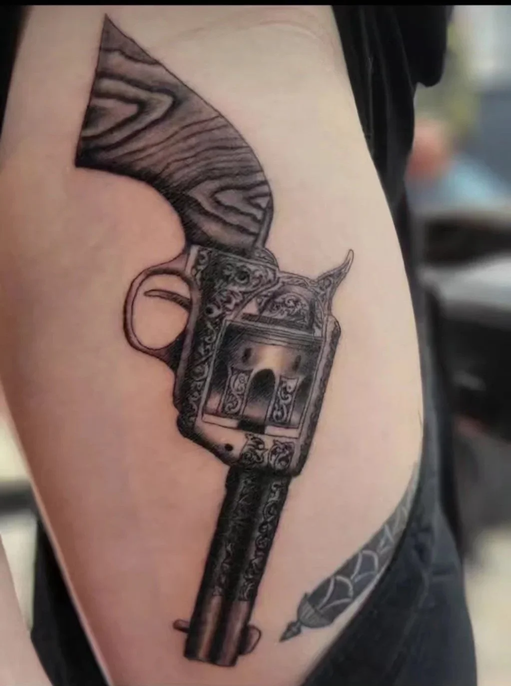 Tattoo of an ornately decorated revolver on person's upper arm.