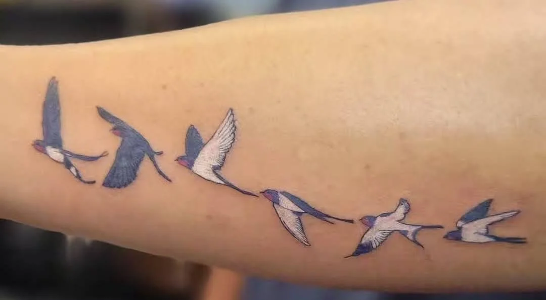 Tattoo of seven birds in flight on a person's arm.
