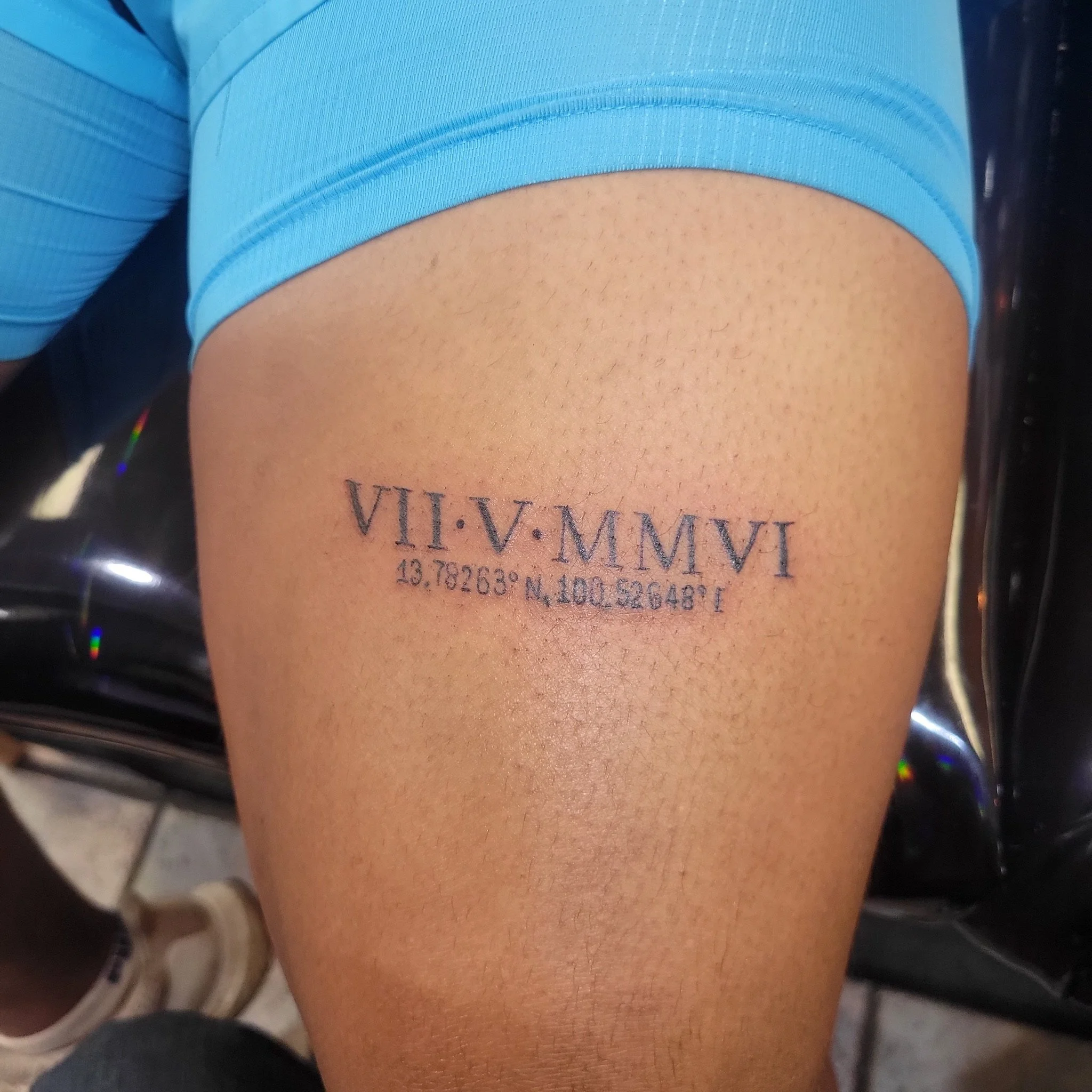 Tattoo on person's thigh with Roman numerals and coordinates.