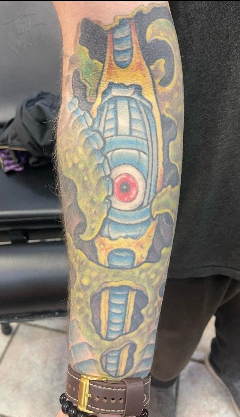 A colorful tattoo on a person's forearm depicting a spaceship surrounded by clouds and smoke, with detailed sci-fi elements and vibrant colors.