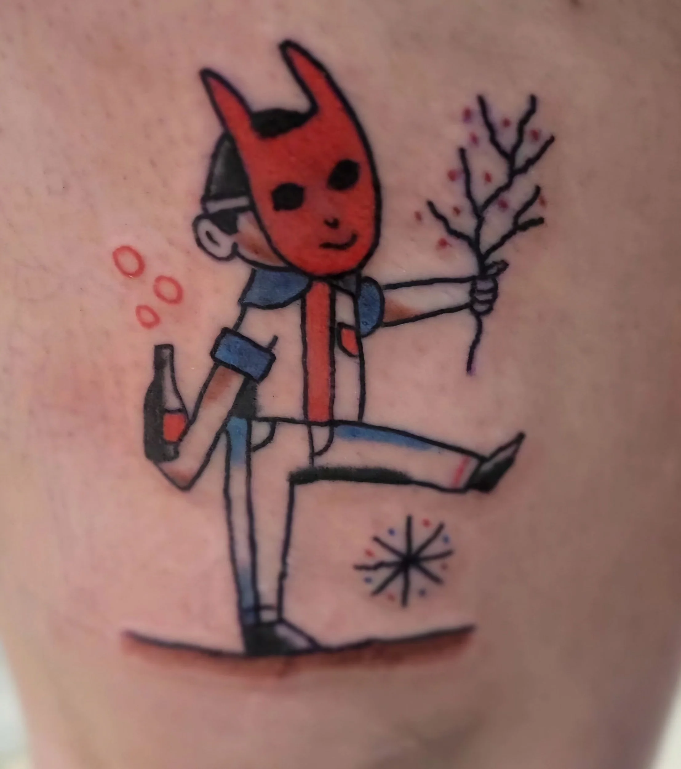 A colorful tattoo of a cartoon boy with a devil mask on his face, holding a small plant in one hand and a bottle in the other, with abstract star and bubble designs around him.