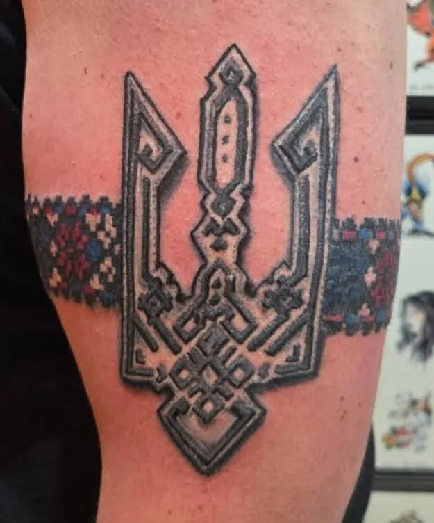 Tattoo of a geometric trident with a decorative band around the arm.