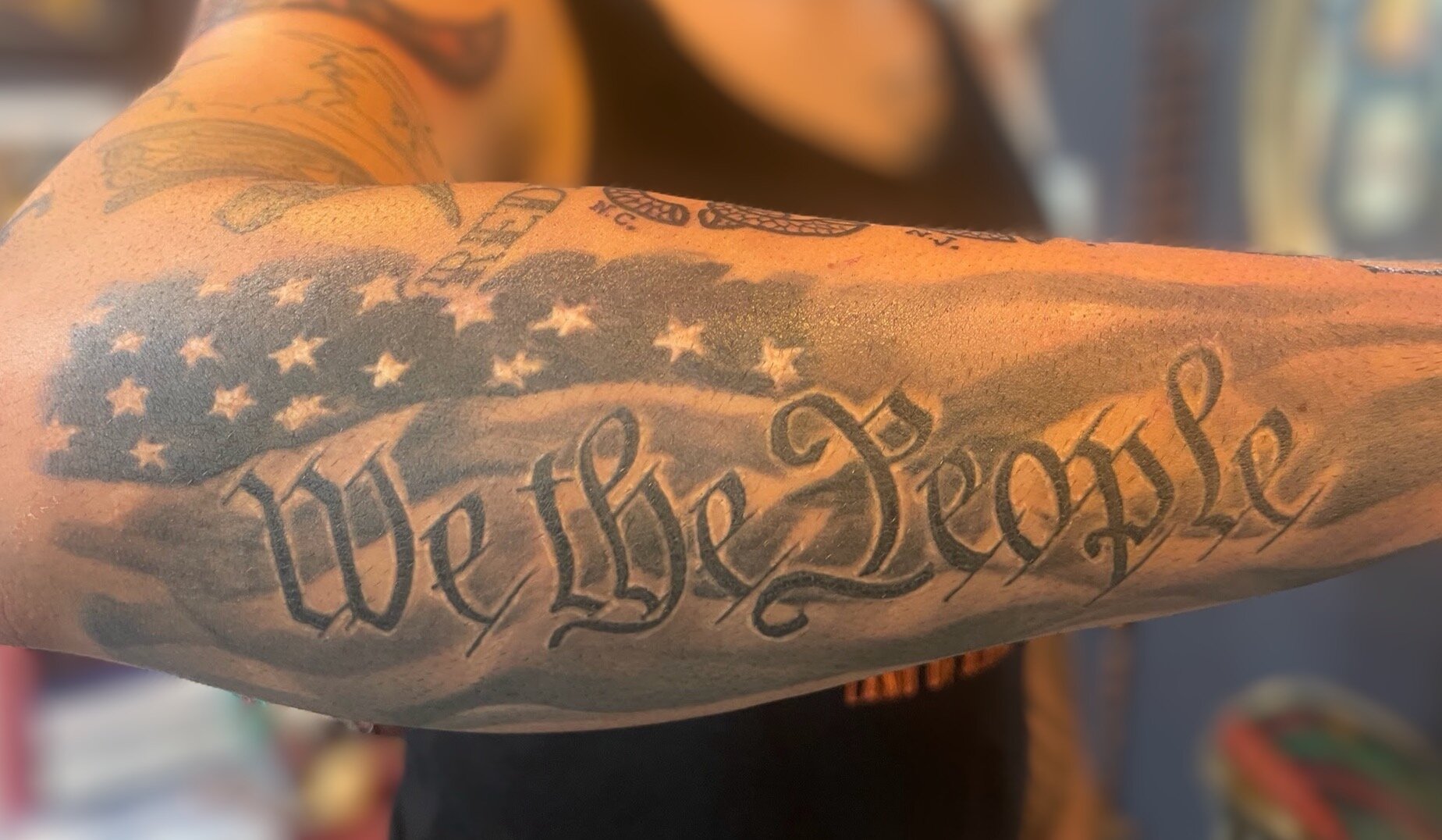 Tattooed arm with the phrase 'We the People' and an American flag on the arm.