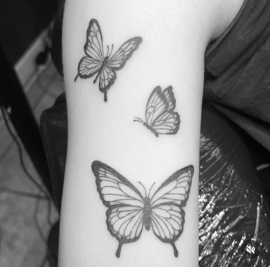 Black and white tattoo of three butterflies on a person's arm.