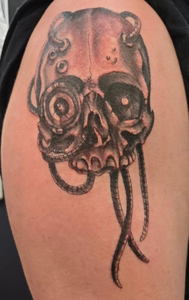 Tattoo of a skull with tentacles and mechanical elements on a person's arm.