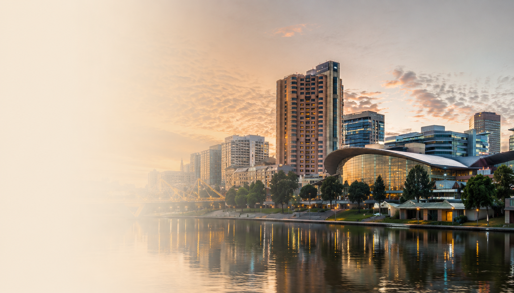 City skyline at sunset with modern buildings and a river reflecting the city's lights.