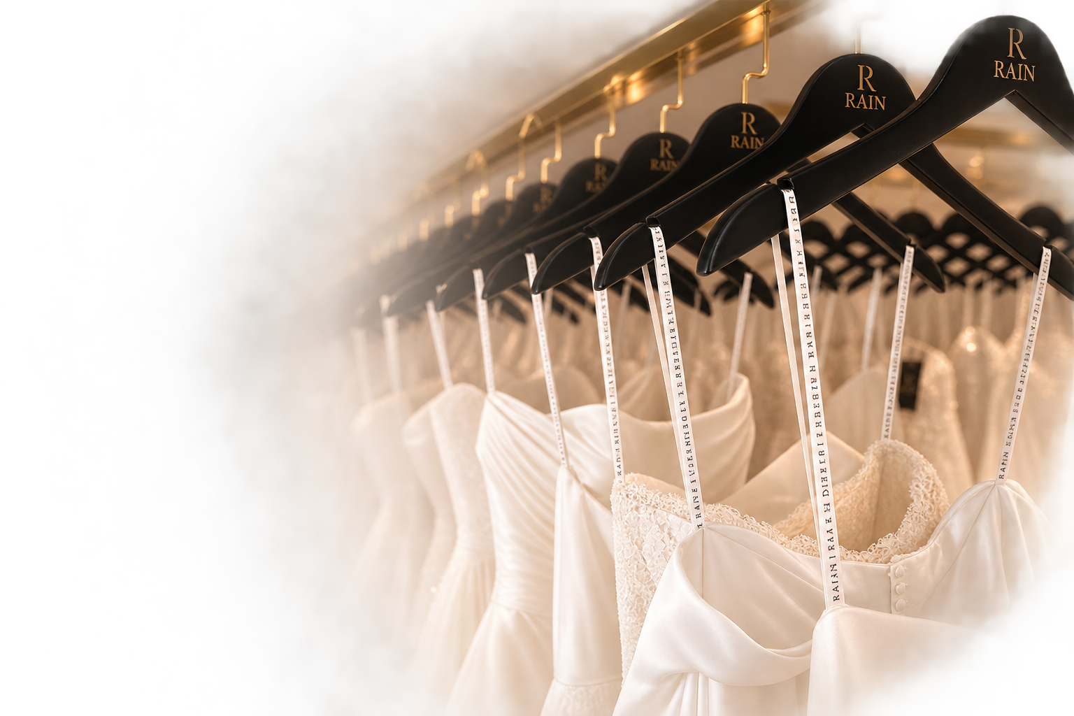 Wedding dresses hanging on black velvet hangers on a metal rod with a gold finish, with a soft light illuminating the dresses.
