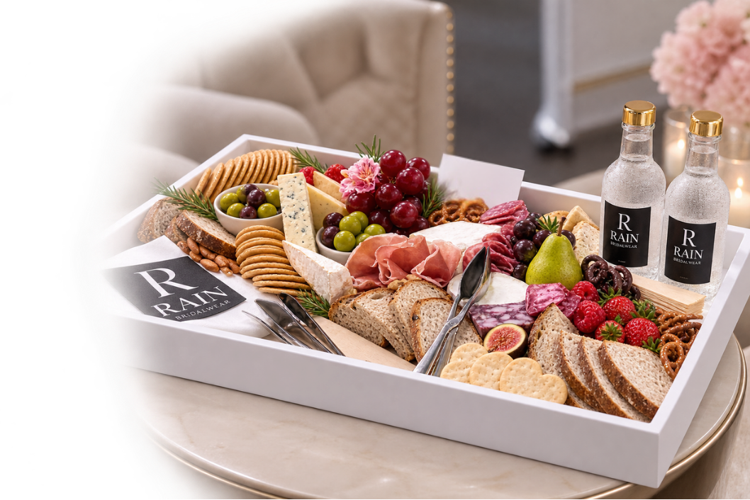 A charcuterie board with crackers, cheeses, grapes, strawberries, figs, ham, salami, and a pear, accompanied by two bottles of water and silver utensils in a formal setting.