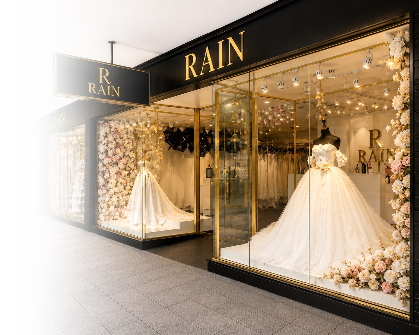 Storefront with wedding dresses on mannequins, decorated with flowers, inside a jewelry shop named RAIN with black and gold signage.