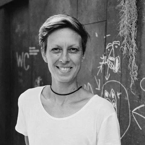 Black and white photo of a woman smiling, standing outdoors in front of a chalkboard with doodles and writing.