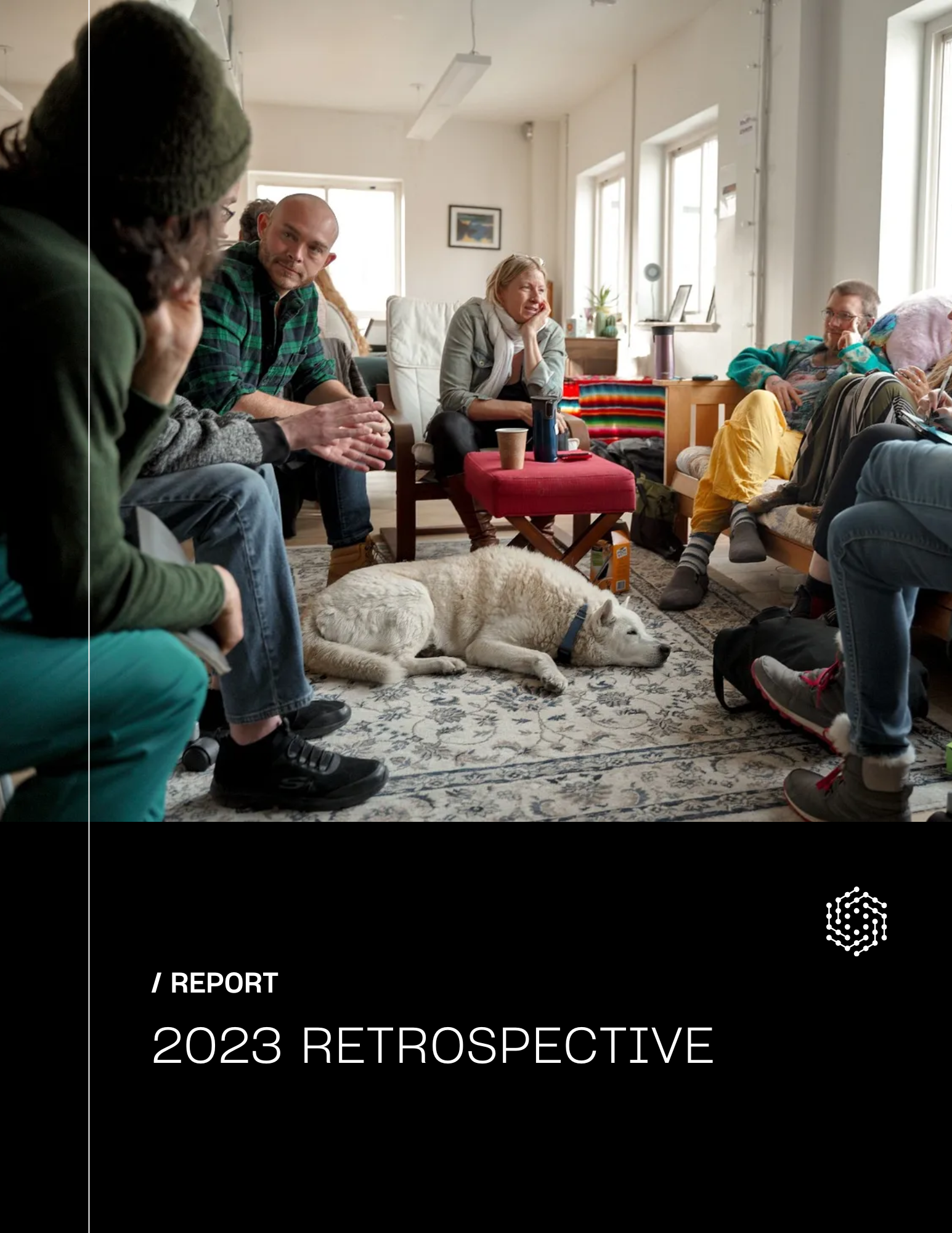 A group of people sitting in a cozy living room, engaged in conversation, with a dog resting on the rug in front of them. Natural light streams through the large windows.