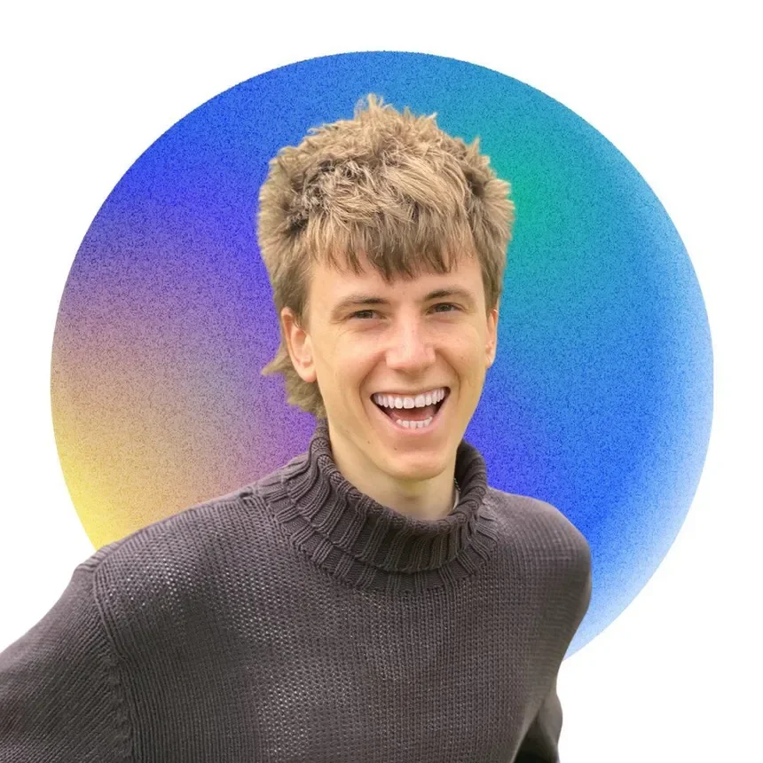 A young man with light brown hair, smiling and wearing a dark gray sweater, standing in front of a circular, multicolored gradient background.