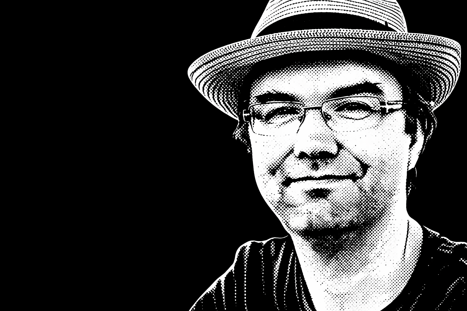 A black and white pixelated portrait of a man wearing a wide-brimmed hat and glasses, smiling slightly against a black background.