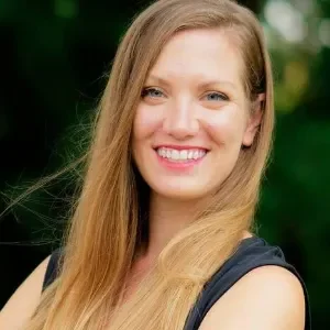 A woman with long blonde hair smiling outdoors, wearing a sleeveless black top.