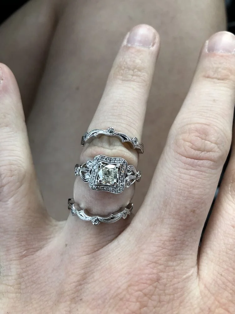 A close-up of a hand wearing three decorative rings with intricate designs and stones, possibly on the ring finger.