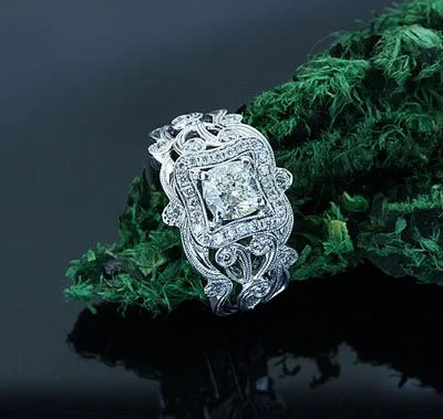 Close-up of an ornate silver and diamond ring resting on a piece of green textured fabric.