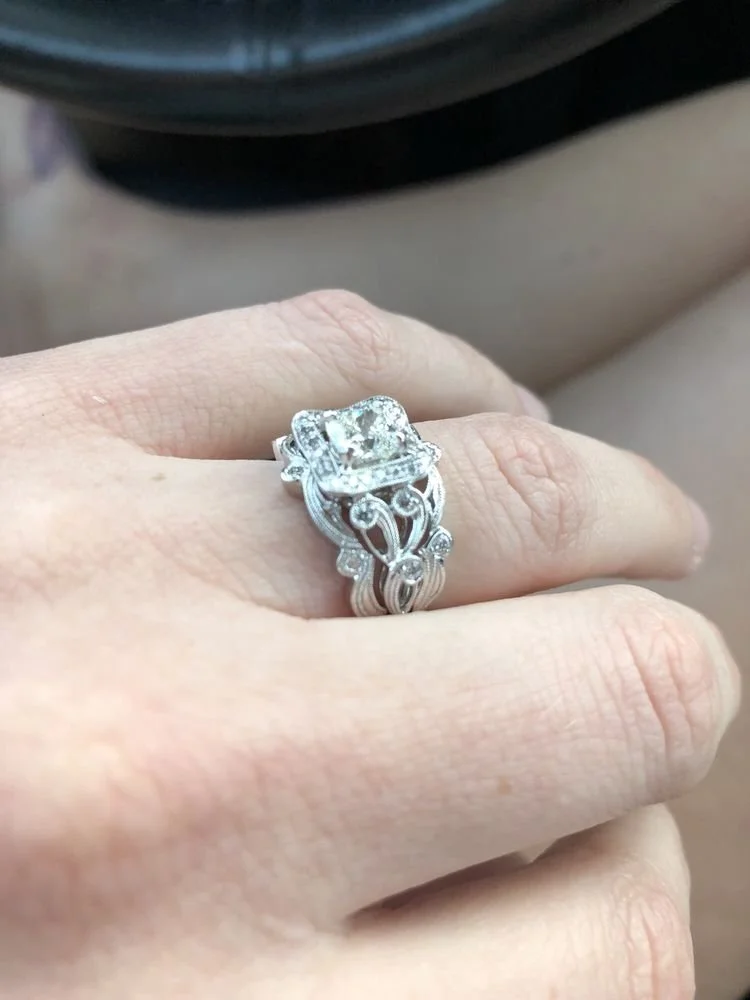 Close-up of a woman's hand wearing a silver ring with intricate designs and a large square-cut diamond center stone.