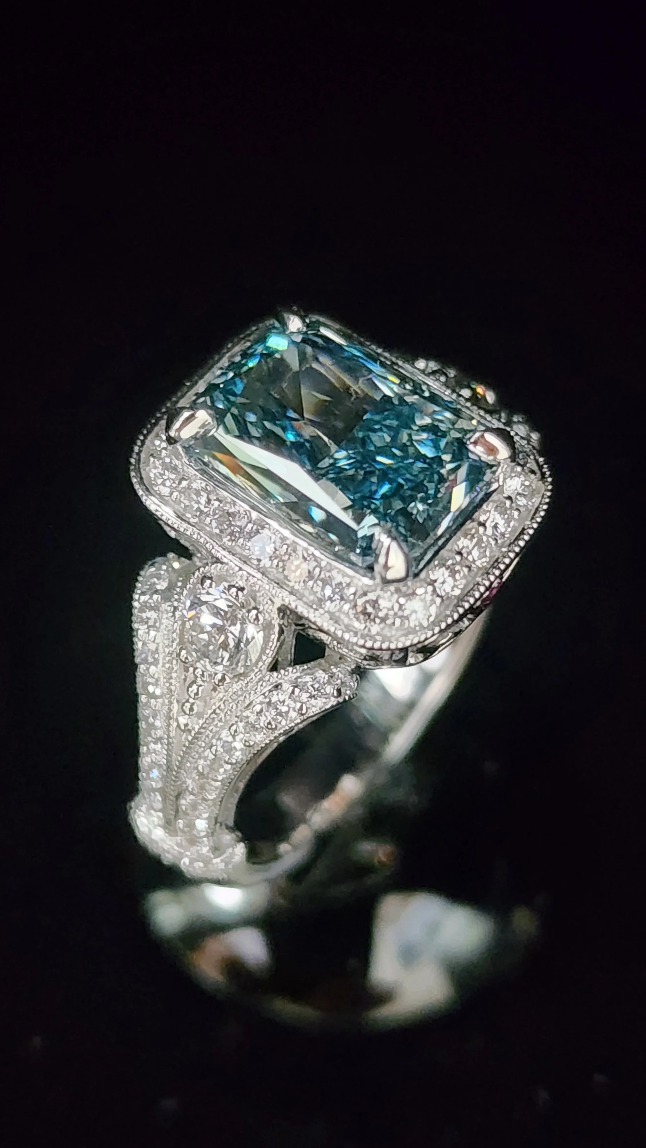 Close-up of a silver ring with a large rectangular blue gemstone surrounded by small white diamonds, with a decorative band also embedded with diamonds.