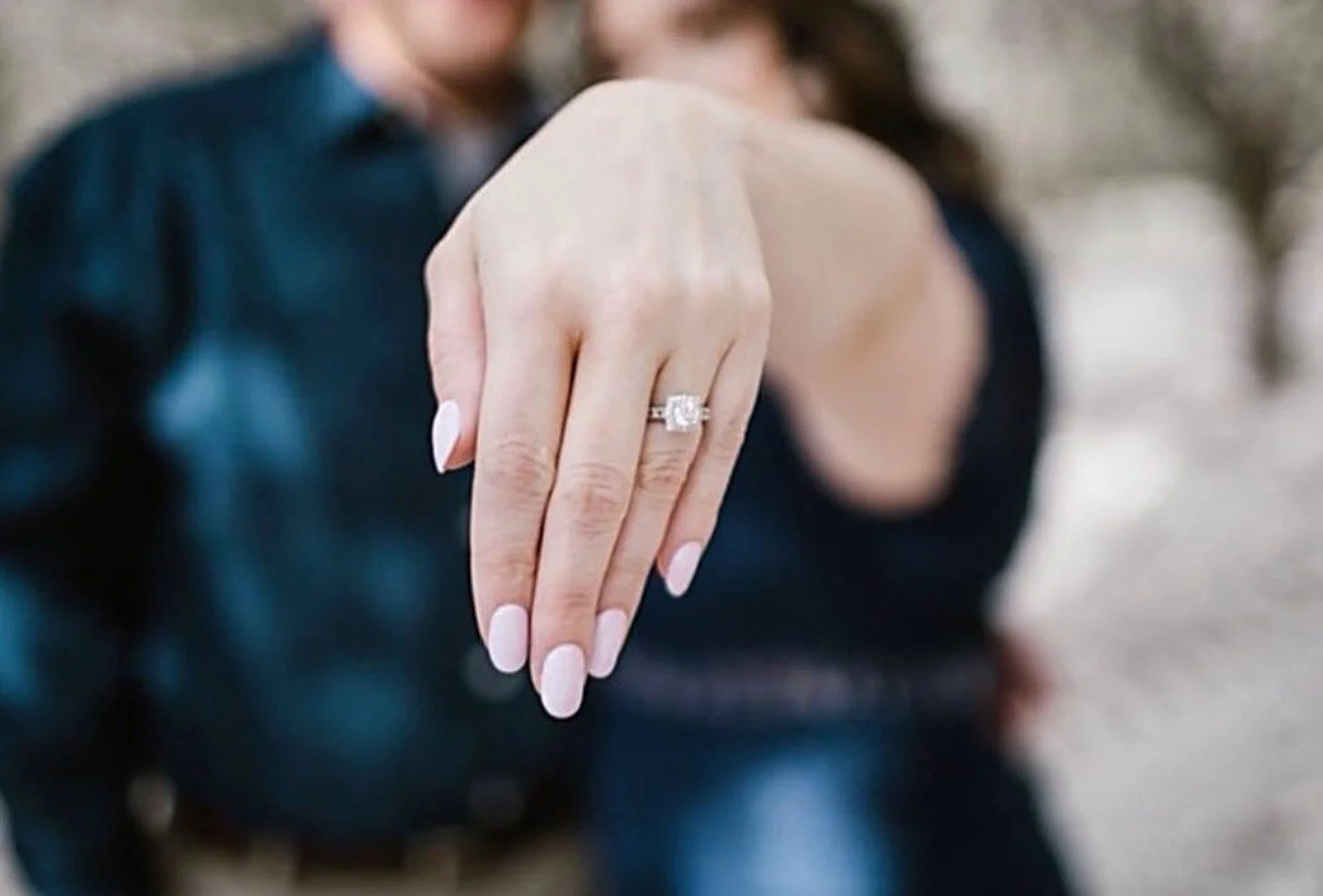 Custom diamond engagement ring with diamond band, shown on the hand of a newly engaged couple, handcrafted by Kaz Jewelry