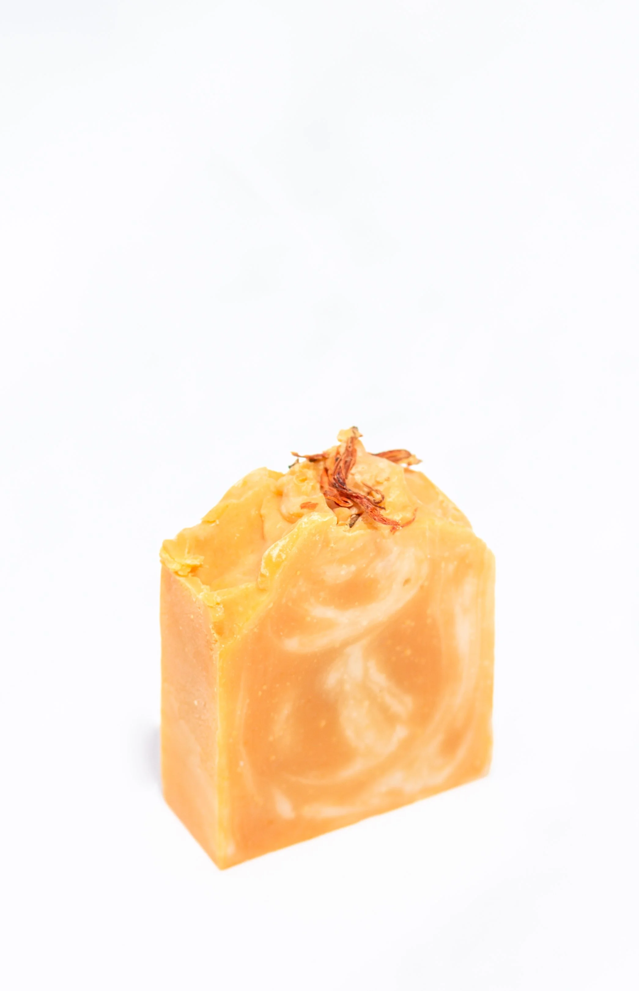 A bar of orange soap with swirls of white and a small dried flower on top against a white background.