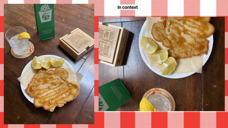Fried fish fillet with lemon wedges, a glass of water with lemon, and a box of hush puppies on a wooden table.