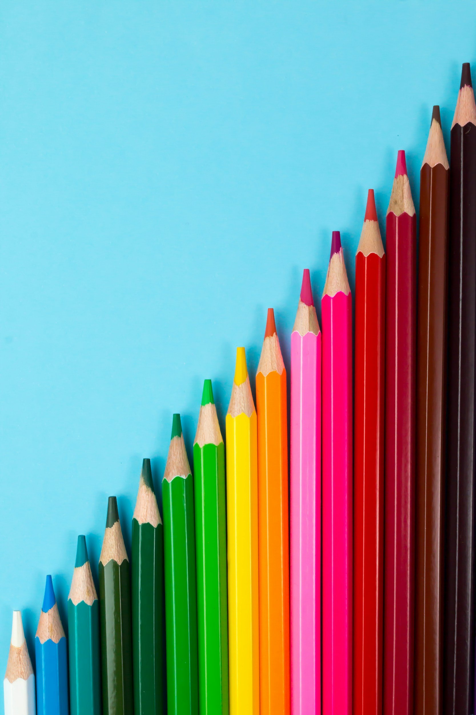 Colorful colored pencils arranged in increasing height against a light blue background.