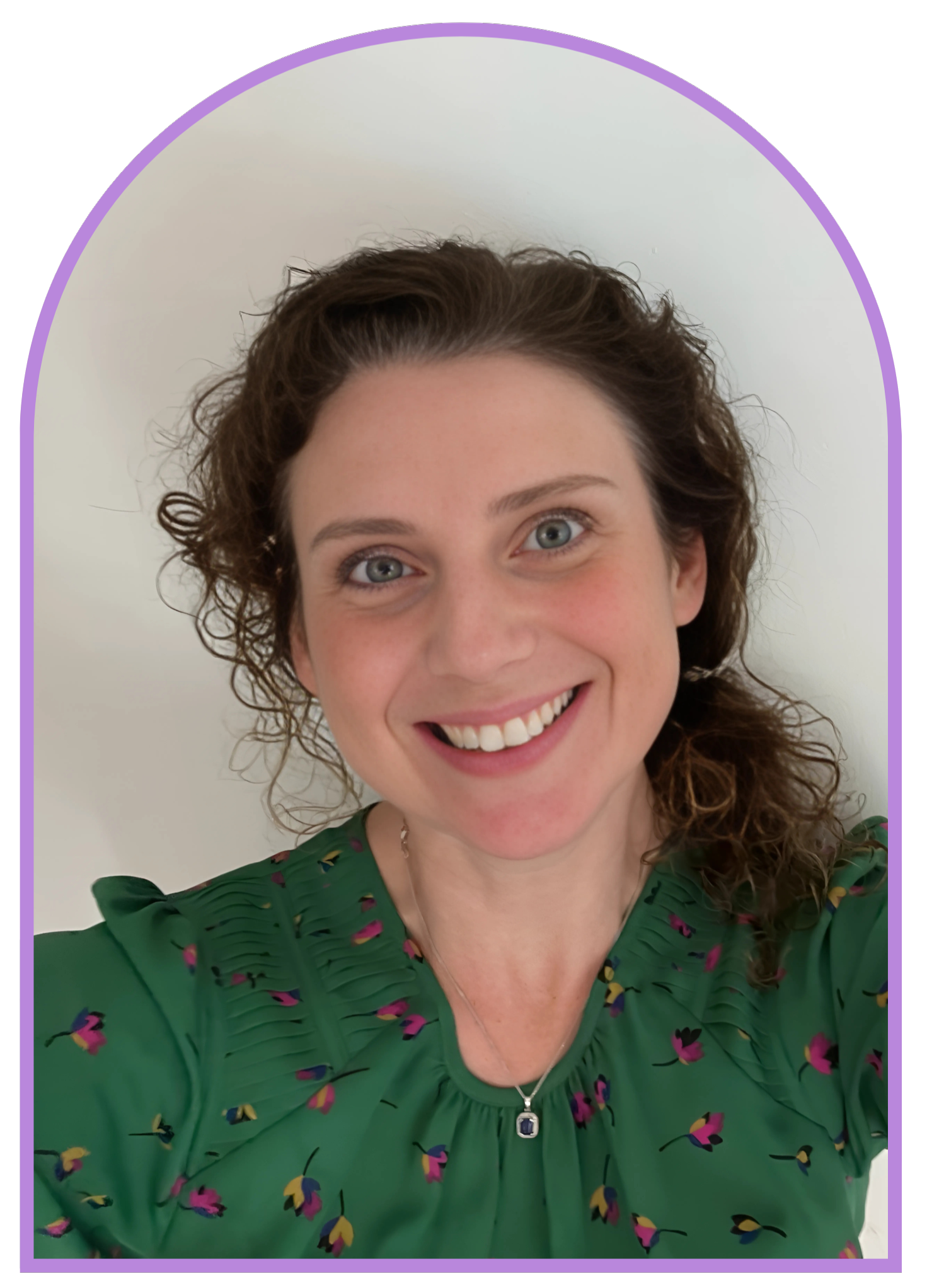 Close-up photo of a smiling woman with curly brown hair, wearing a green floral top and a necklace with a blue gemstone pendant, against a white background.