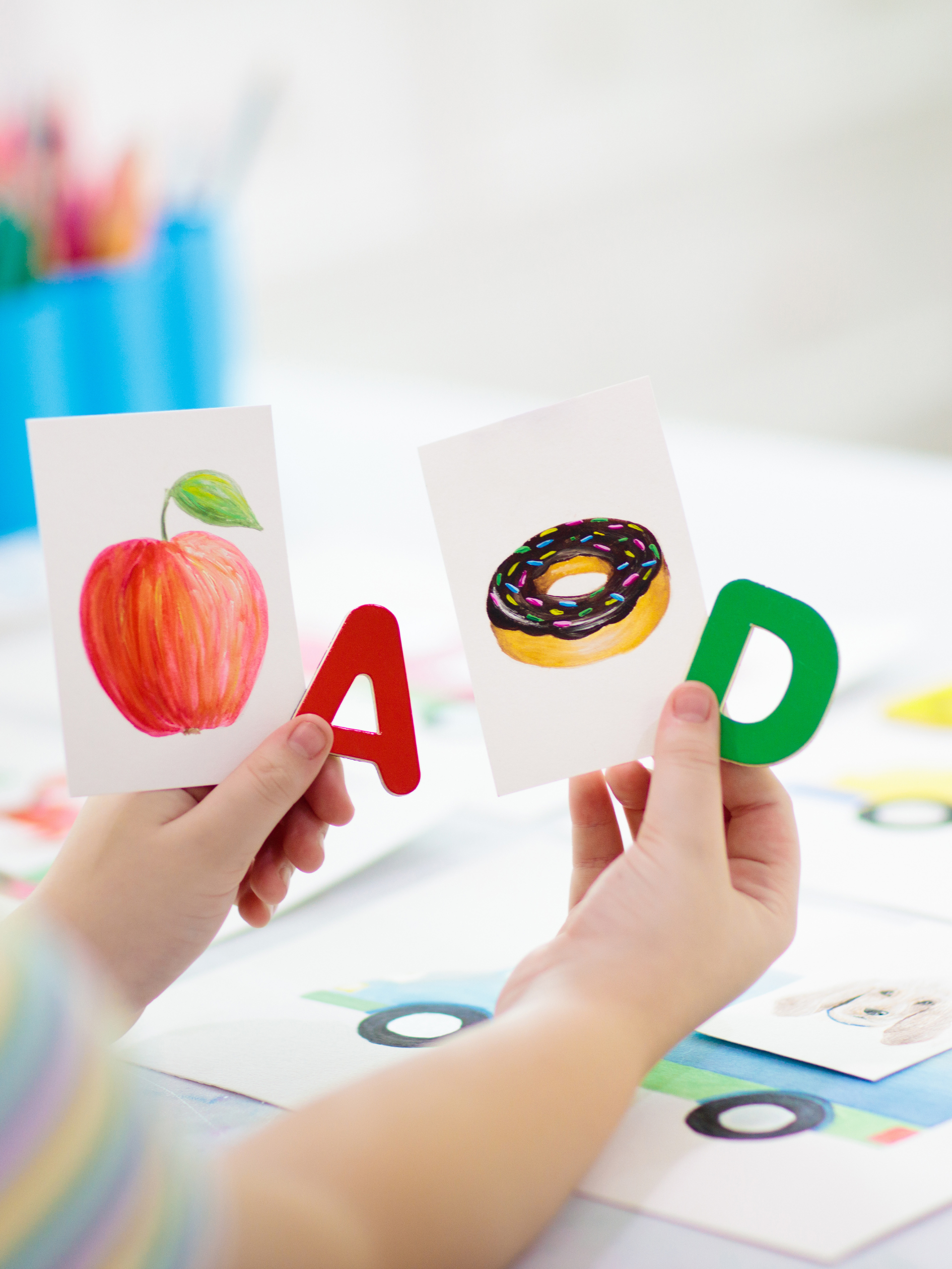 Child holding cards with images of a peach and a donut, with large red 'A' and green 'D' letters.