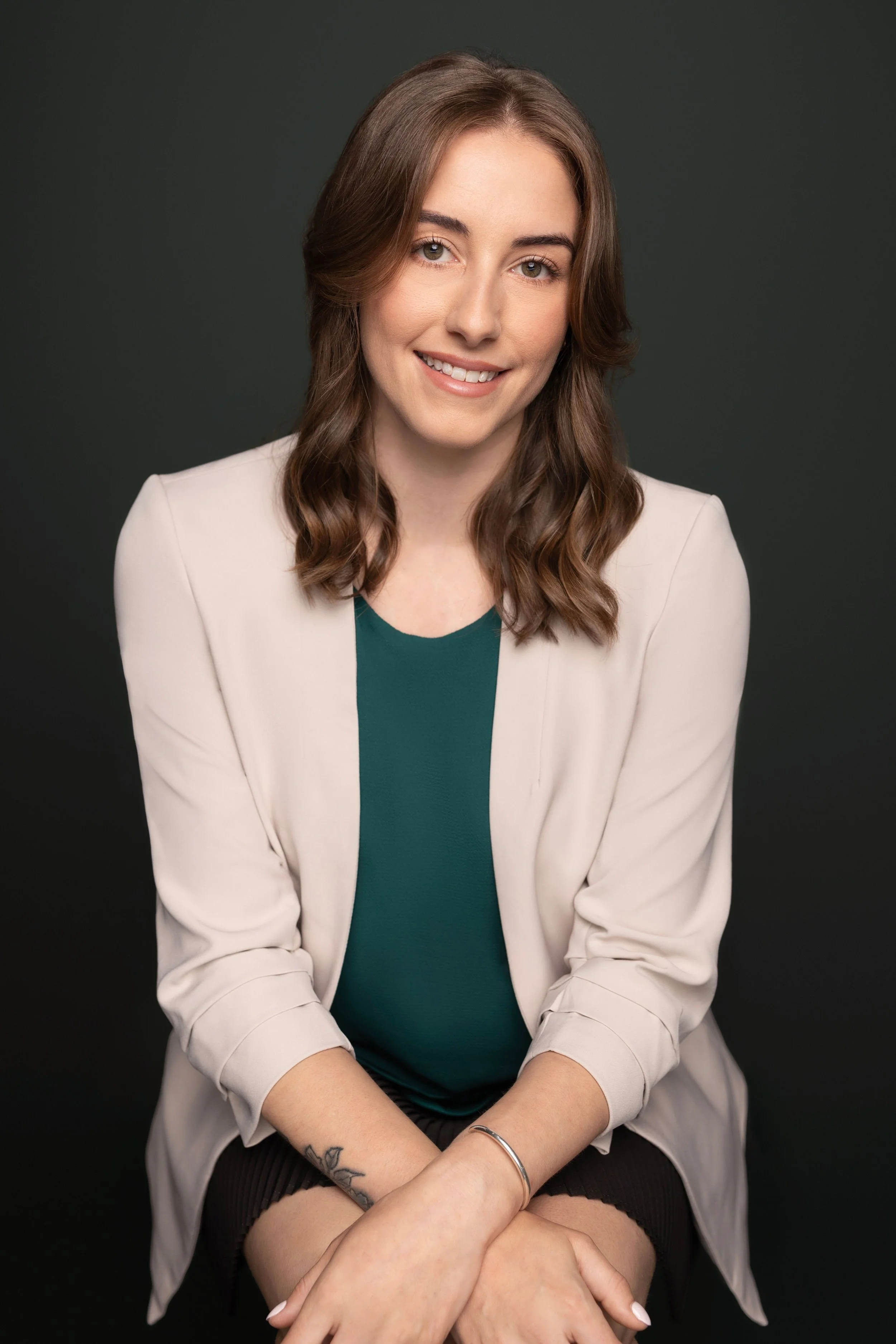 A young woman with brown, wavy hair smiling while sitting against a dark background.