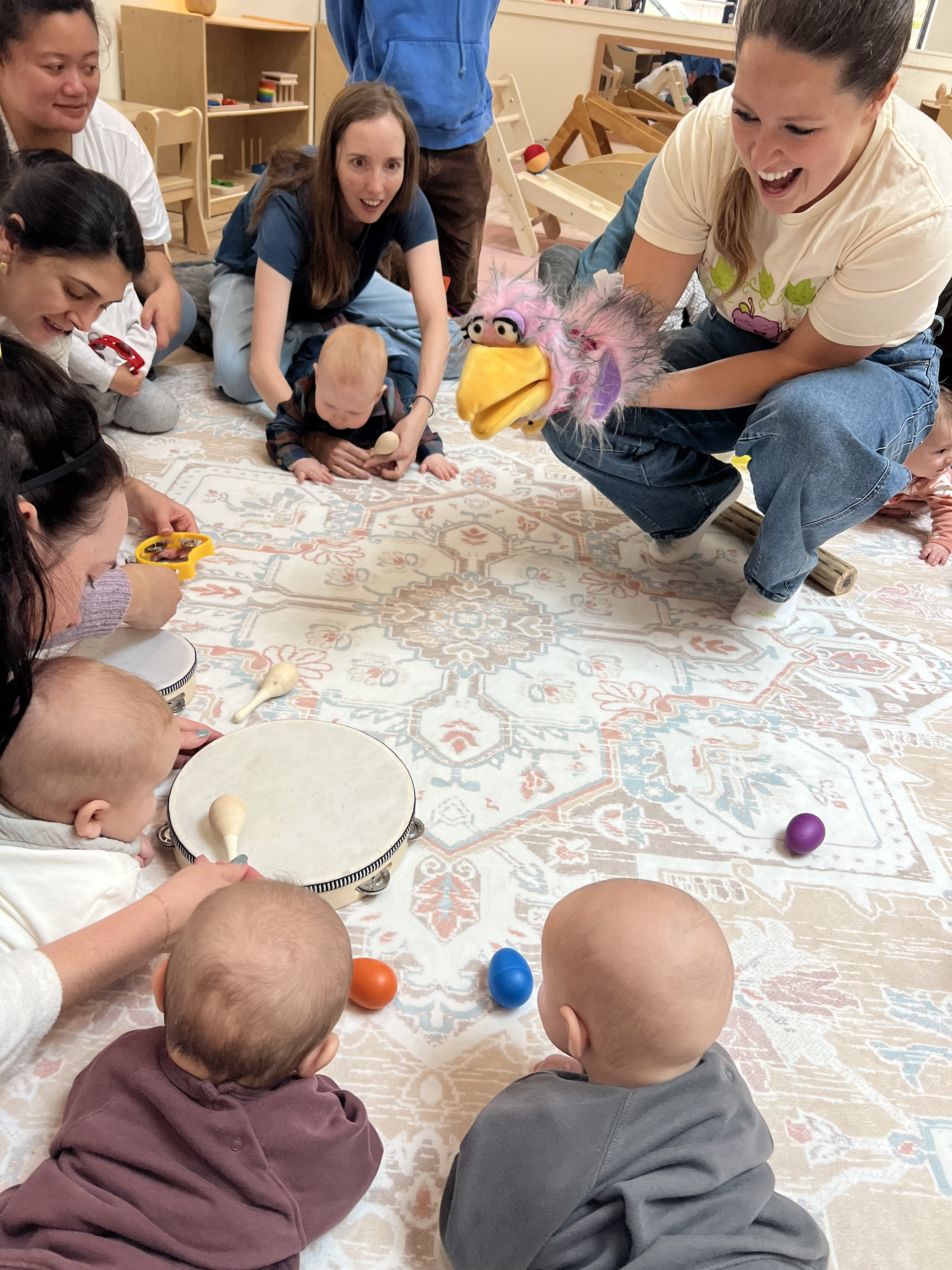 A young child with blonde hair sitting on a black and white geometric patterned rug, holding a red star-shaped balloon with their reflection visible on the balloon.