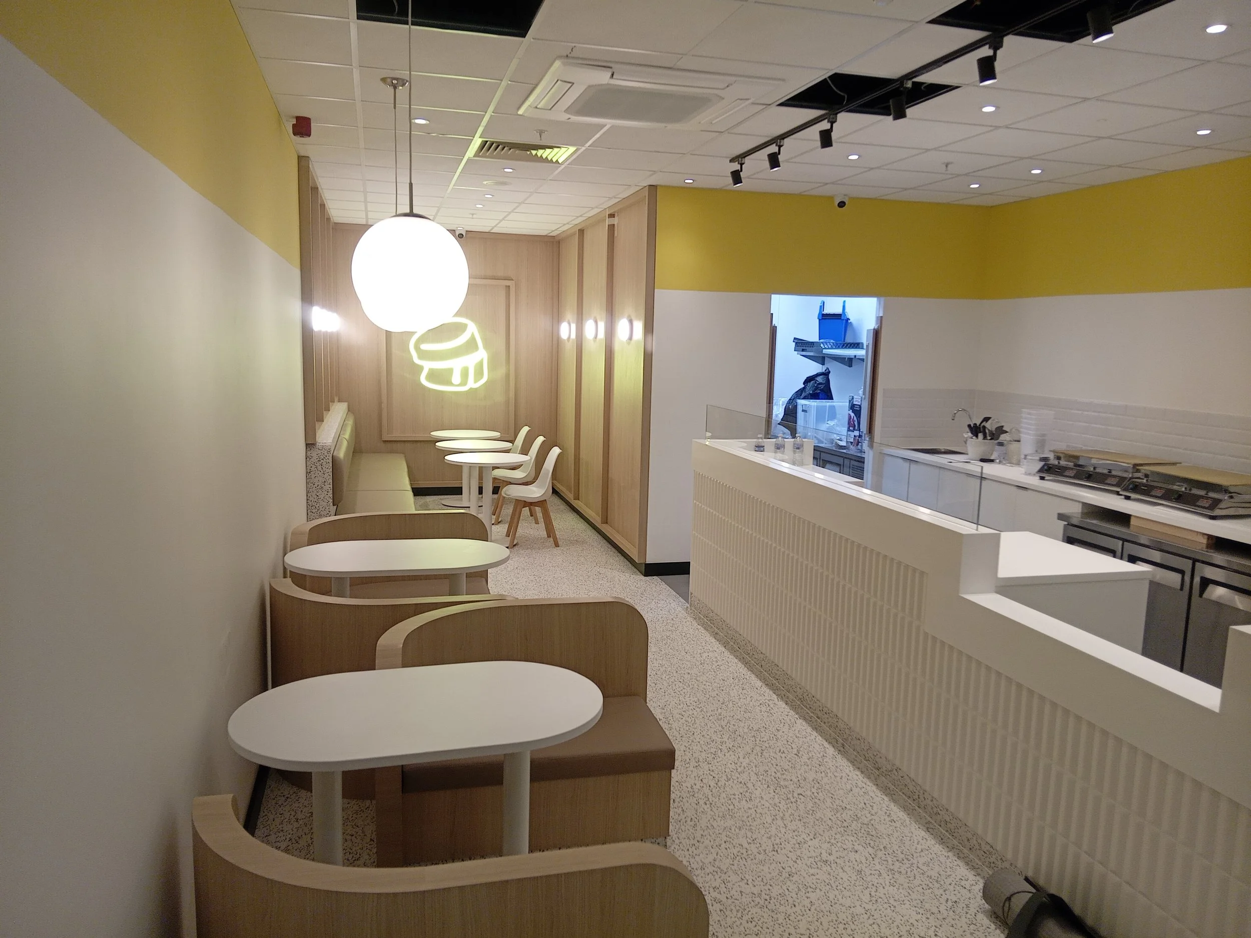 Empty dining area with white tables and wooden chairs, modern decor, and a counter area in the background.